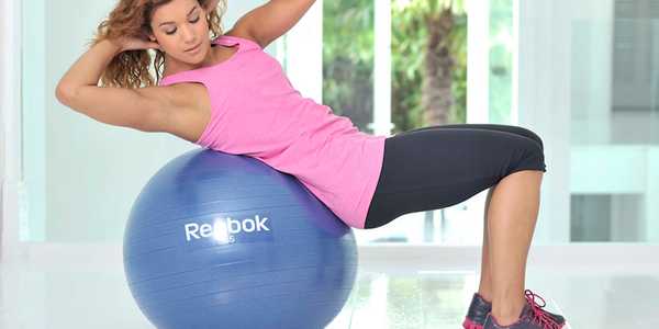 A woman working out at home using a gym ball.